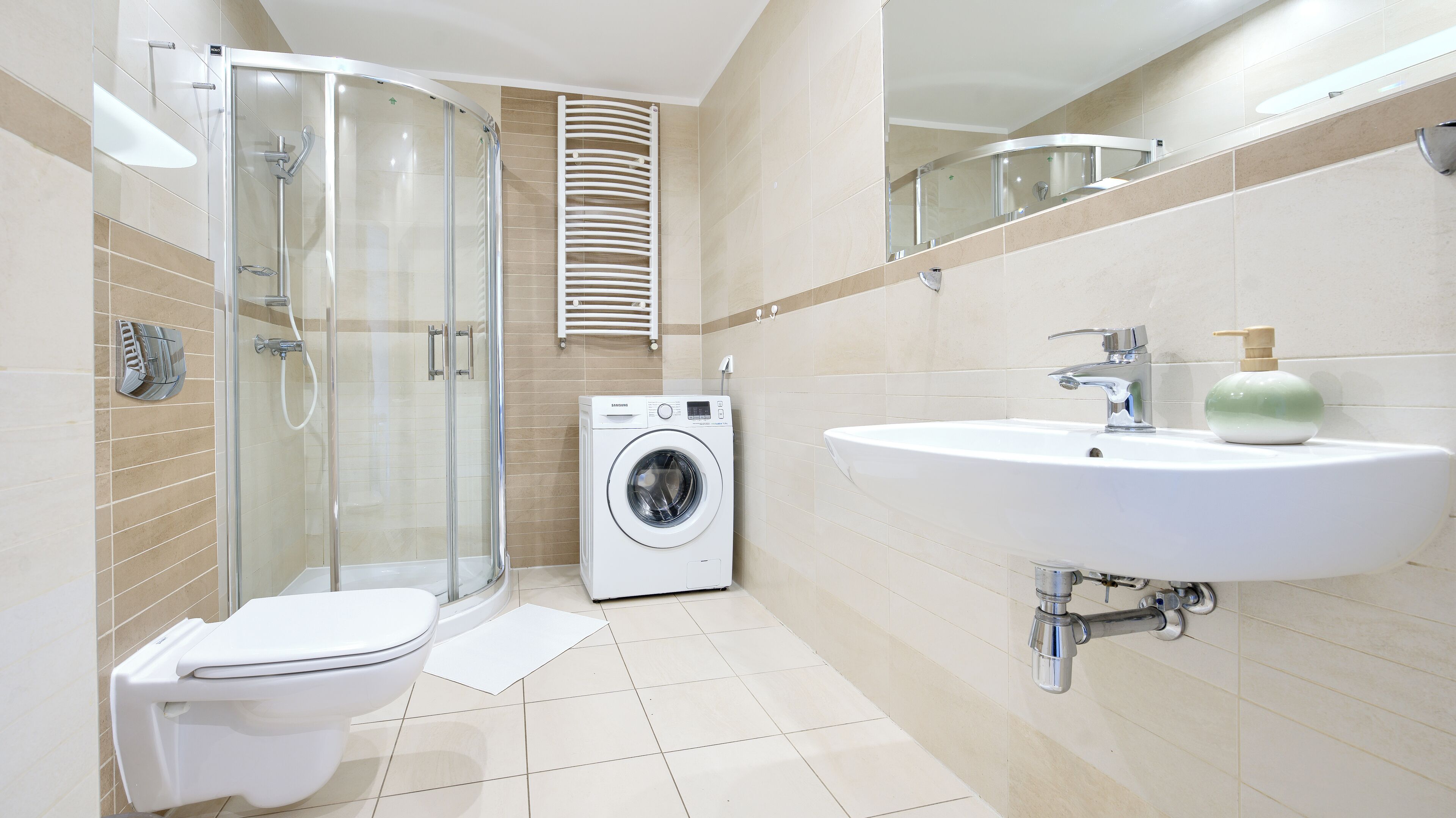 A modern bathroom with a glass shower enclosure, a built-in washing machine, and a sink with a soap dispenser.