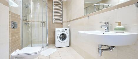 A modern bathroom with a glass shower enclosure, a built-in washing machine, and a sink with a soap dispenser.