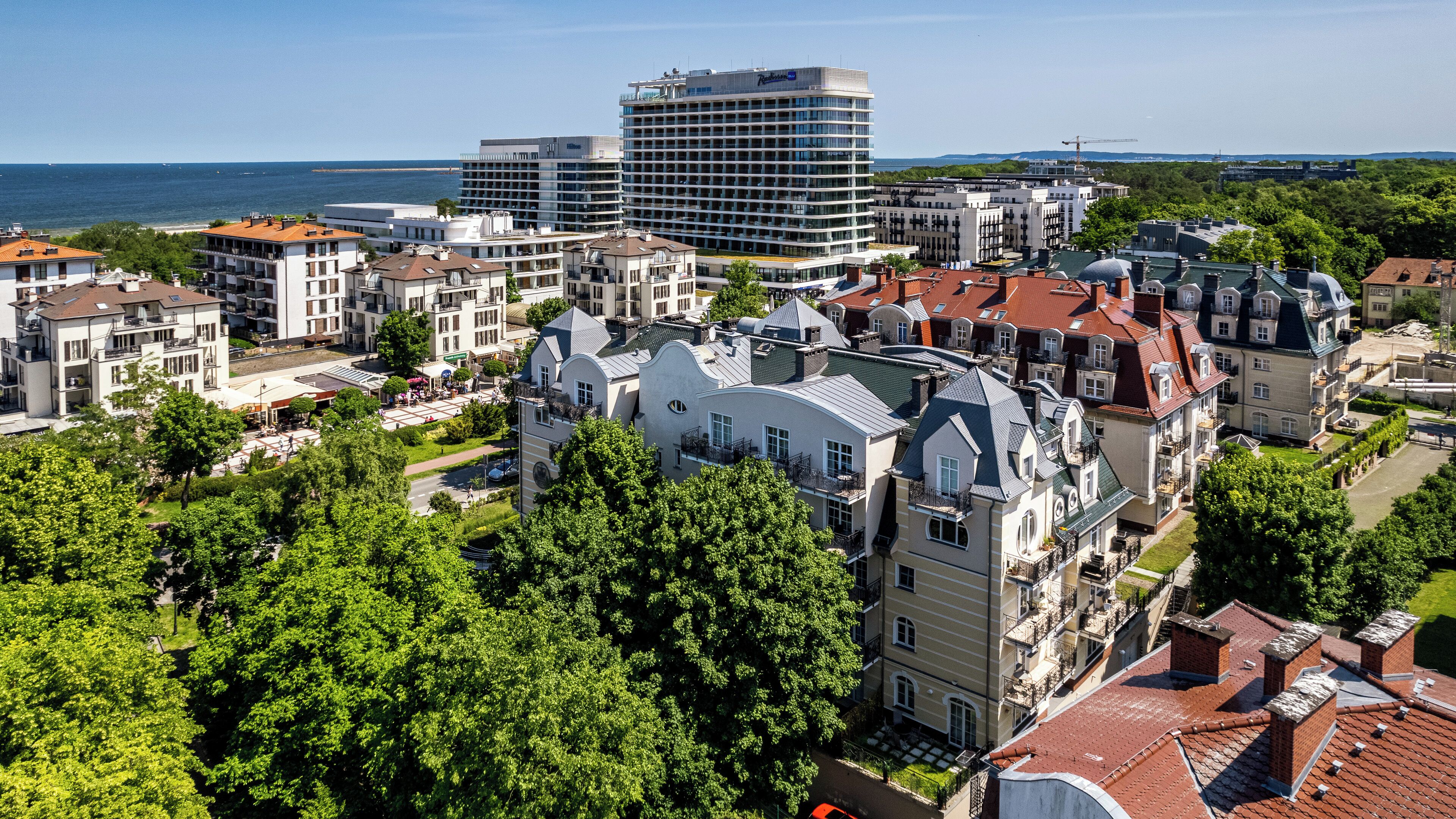 Un paysage urbain côtier, avec un mélange de bâtiments modernes et historiques, dont un hôtel imposant doté de balcons et offrant une vue sur la mer.