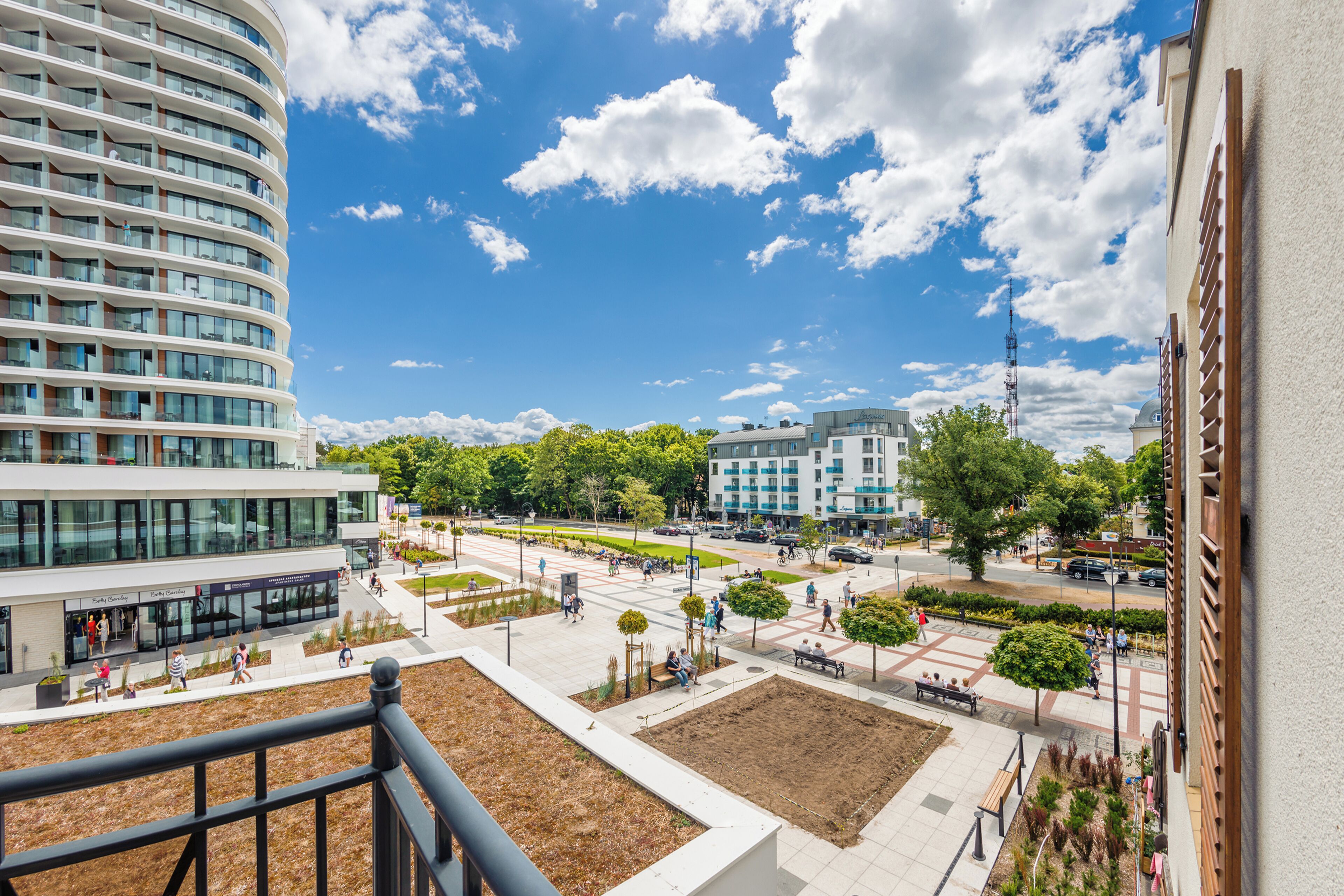 Une place urbaine moderne, dominée par un grand bâtiment à la façade incurvée et comportant plusieurs étages.
