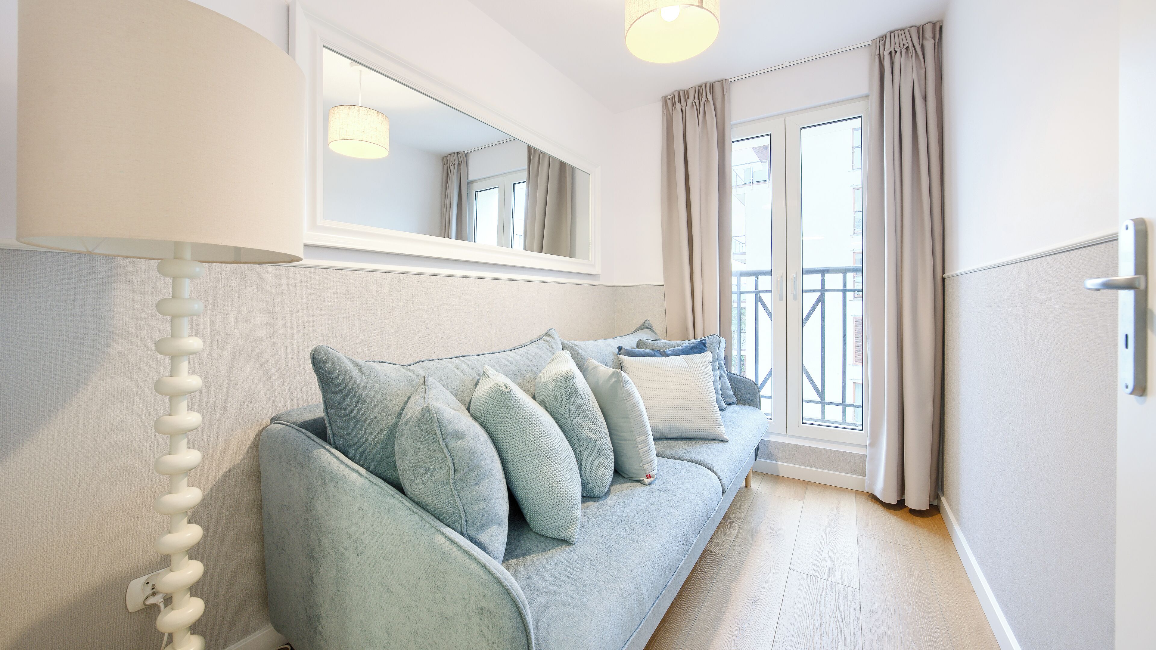 Ein modernes Wohnzimmer mit einem hellblauen Sofa, einem Spiegel darüber und Blick durch große Fenster ins Freie.