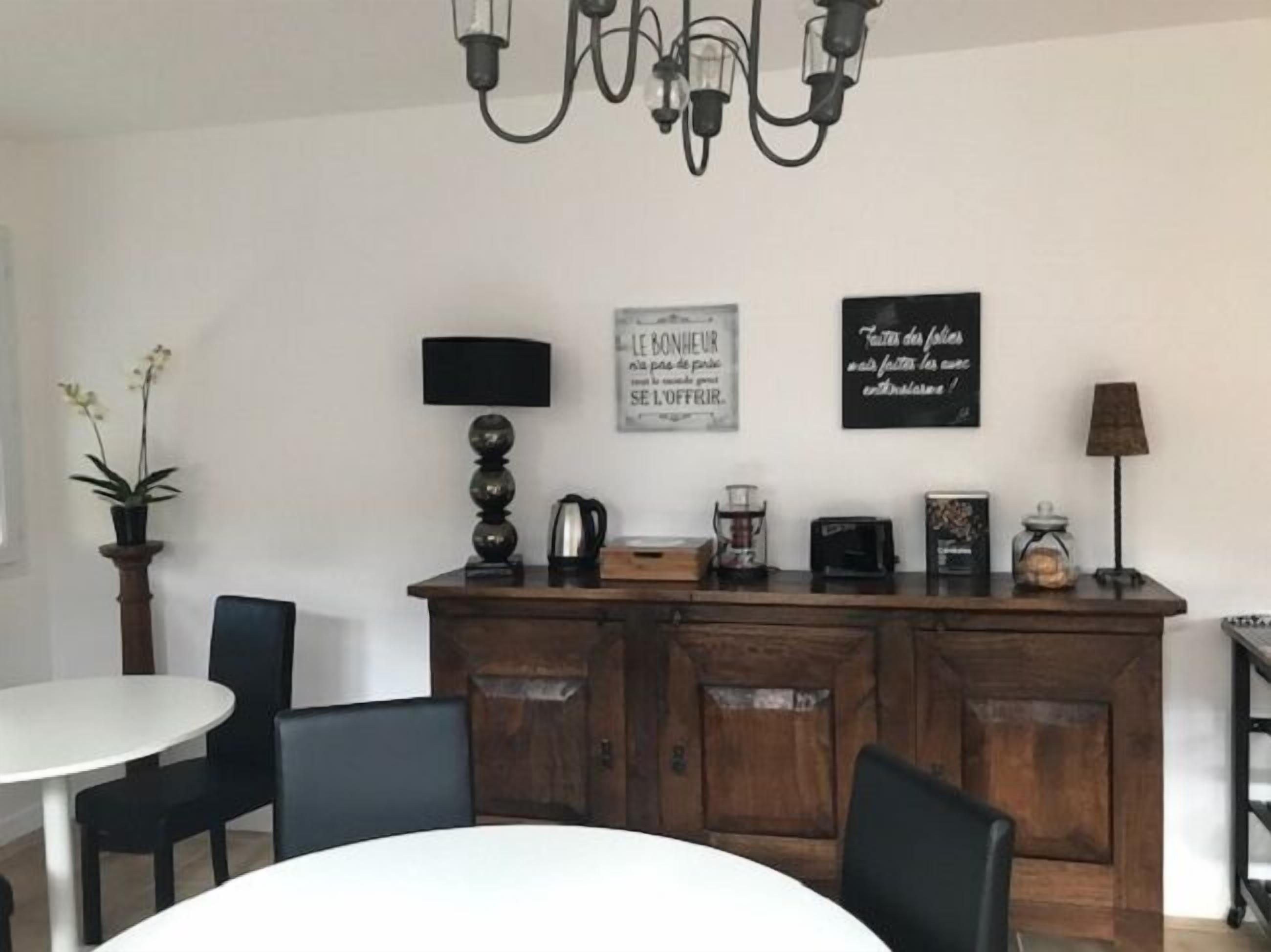 Un comedor con una mesa y sillas blancas, un mueble de madera con electrodomésticos de cocina y dos letreros en la pared.
