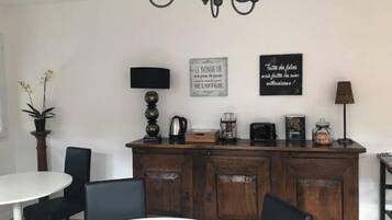 Un comedor con una mesa y sillas blancas, un mueble de madera con electrodomésticos de cocina y dos letreros en la pared.