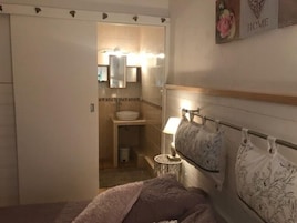 Un dormitorio con cama, mesita de noche, lámpara y baño visible a través de una puerta abierta.
