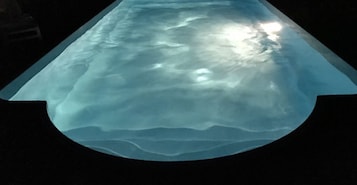 Una piscina con borde ondulado y una fuente de luz reflejada en la superficie del agua.