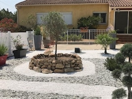 Una casa con techo de tejas, una decoración de jardín de piedra y plantas en macetas.
