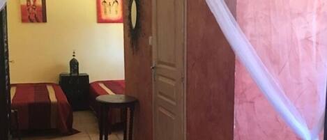 Una habitación con una cama, una mesita y una silla. Se observa una puerta y una pared con un cuadro.
