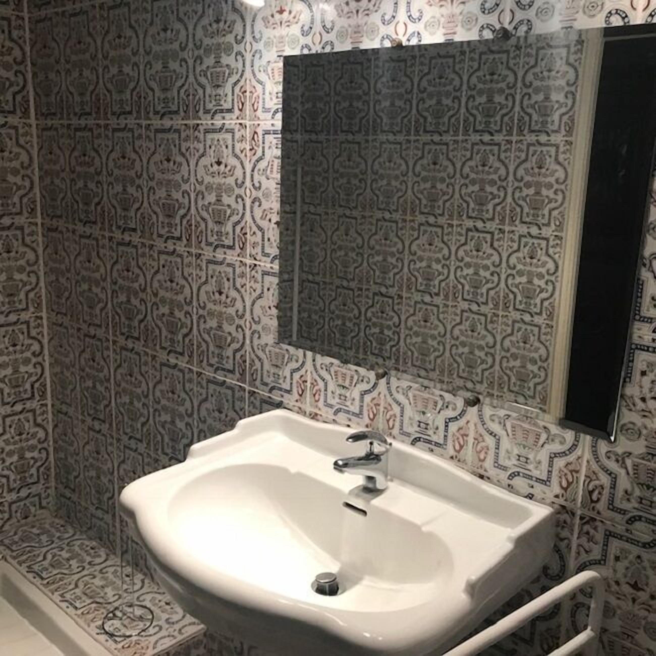 A bathroom with patterned tiles, a white sink, and a mirror.
