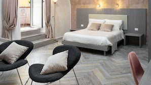 A modern bedroom with a bed, two chairs, a nightstand, and a view of the outdoors. - Toledo Lifestyle (Naples)