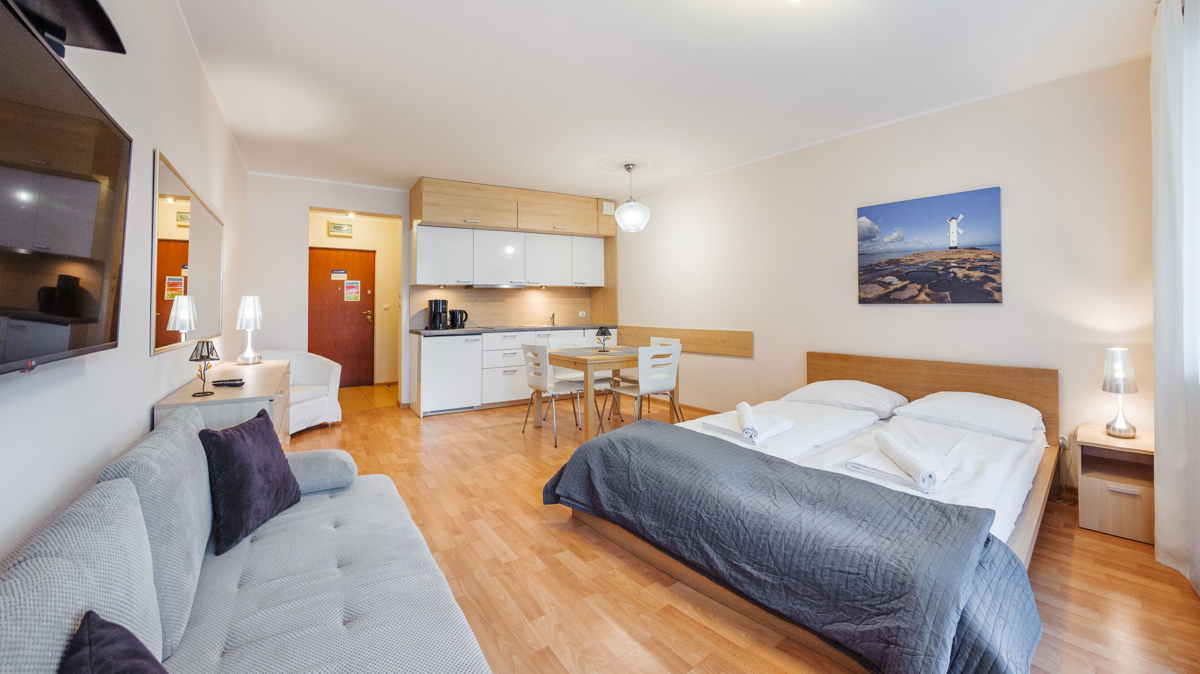 Una habitación de hotel moderna con una cama, un sofá, una mesa de comedor con sillas, una zona de cocina y un cuadro en la pared.