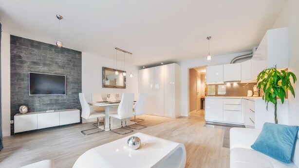 Ein modernes Wohnzimmer mit Flachbildfernseher, weißen Möbeln und einem Essbereich mit Tisch und Stühlen.