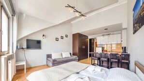Ein modernes Hotelzimmer mit einem großen Bett, einer Sitzecke, einem Essbereich und einer Küche im Hintergrund.