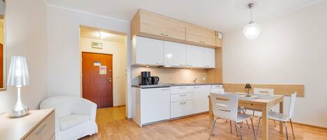 Una cocina compacta con armarios blancos, una cafetera y una mesa de comedor con sillas.