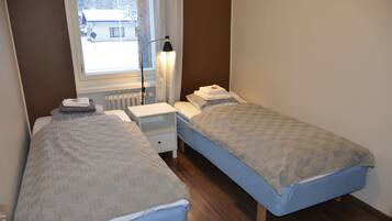 A bedroom with two beds, a nightstand, a lamp, and a window with a view of a building outside.