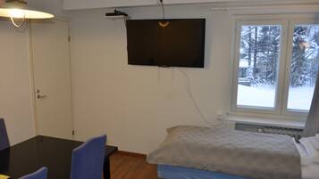 Una habitación con cama, una mesa con sillas, un televisor fijado en la pared y una ventana con vistas a árboles cubiertos de nieve.