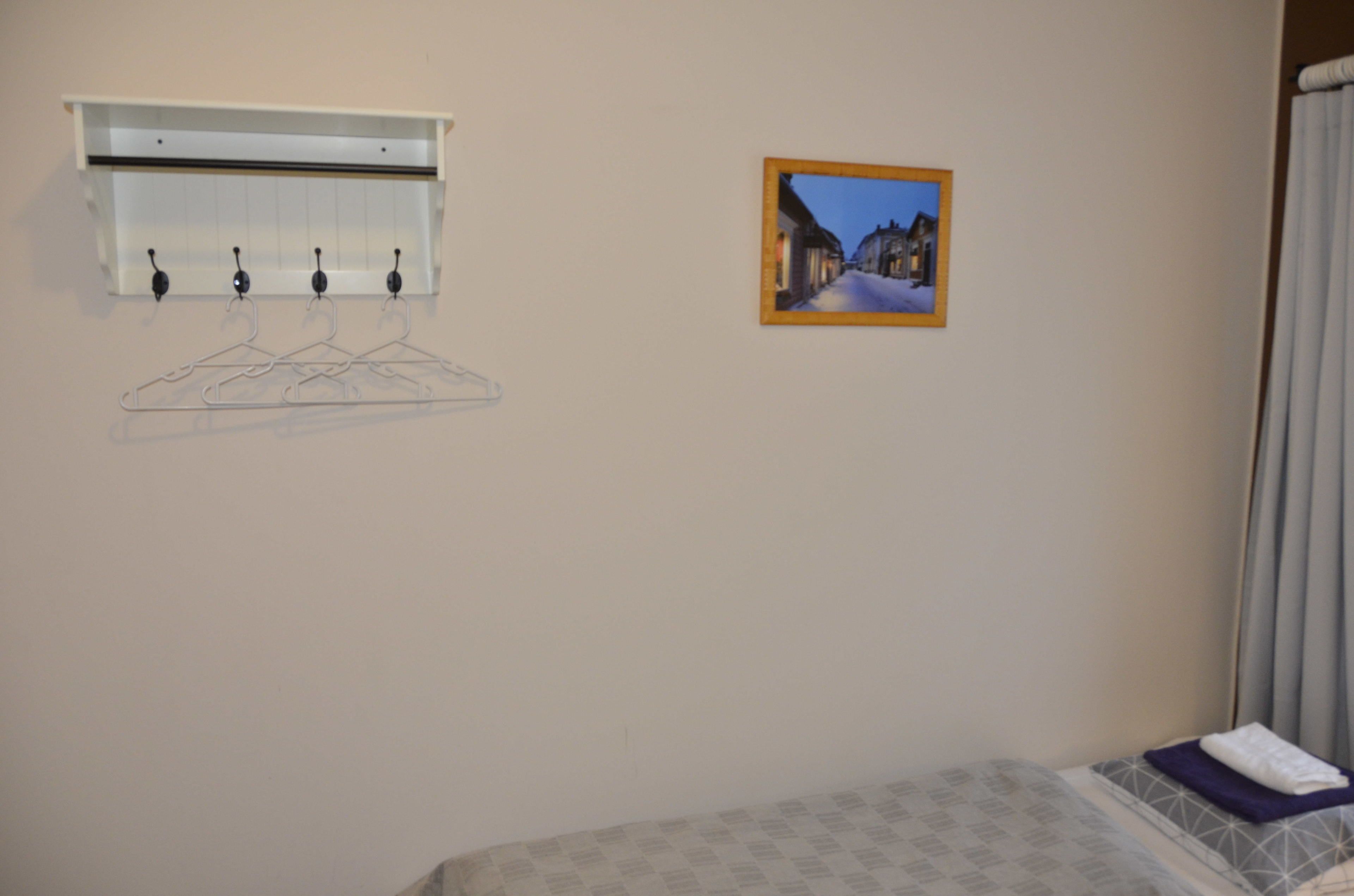 A hotel room with a bed, a coat rack with hangers, a picture on the wall, and a window with curtains.