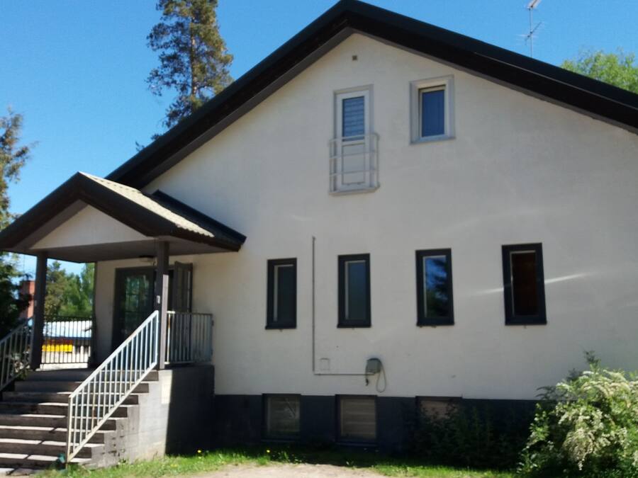 A two-story building with a white exterior and dark trim. It features a set of stairs leading to a covered porch with a railing.