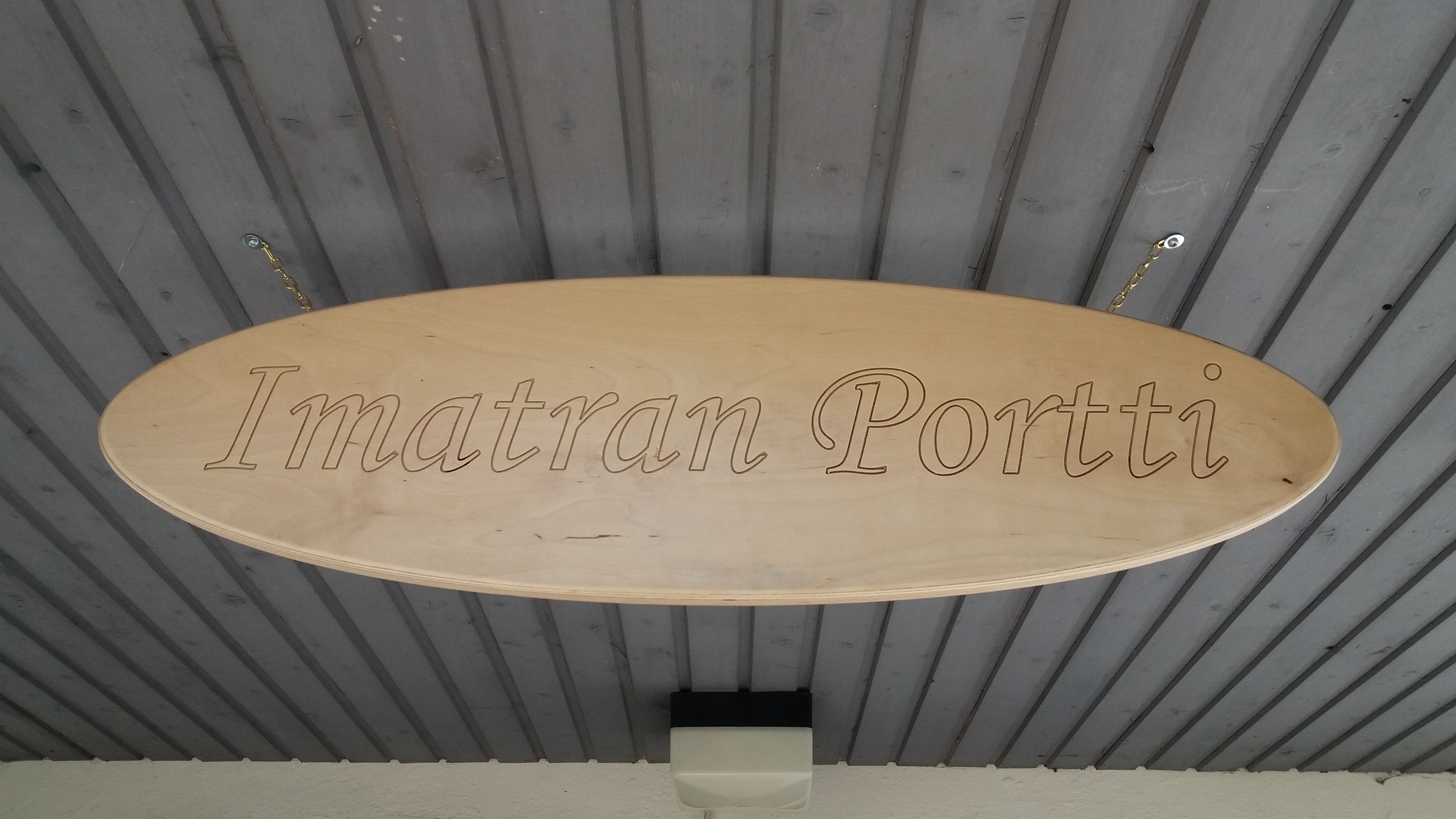 A wooden sign with the inscription "Imatran Portti" against a corrugated metal ceiling.