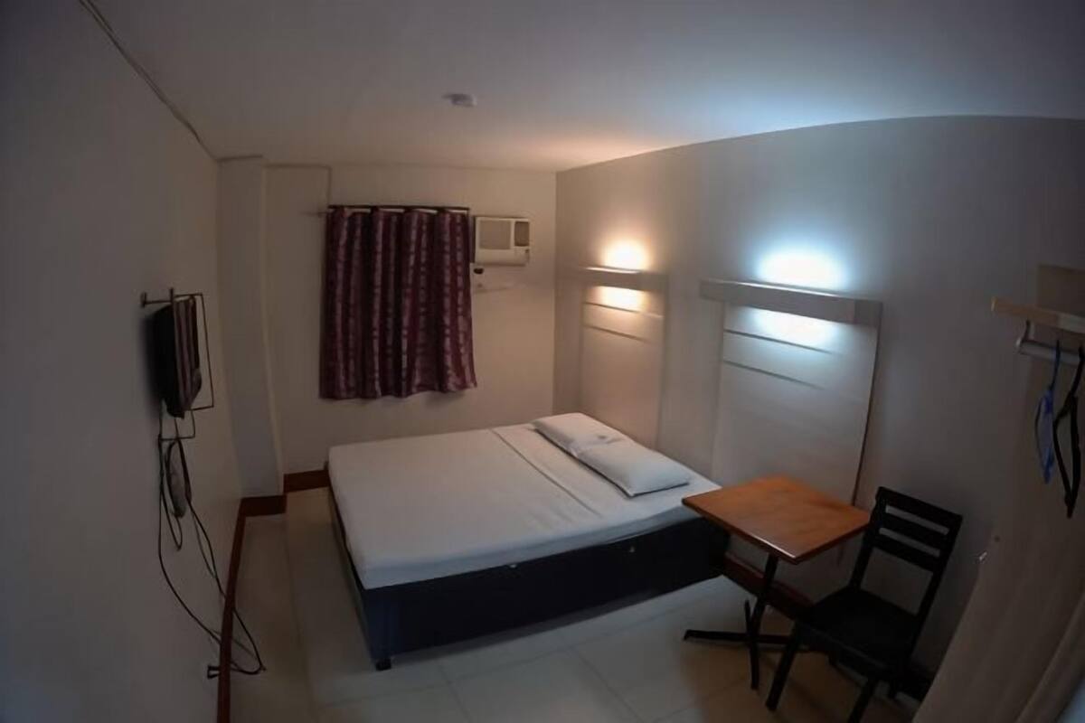 A small, single-bed room with a desk and chair, a television, and a curtain.