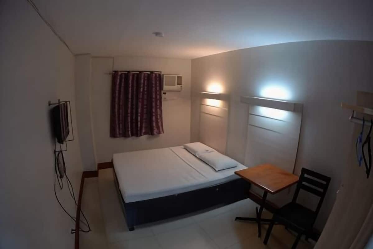 A small, single-bed room with a desk and chair, a television, and a curtain.
