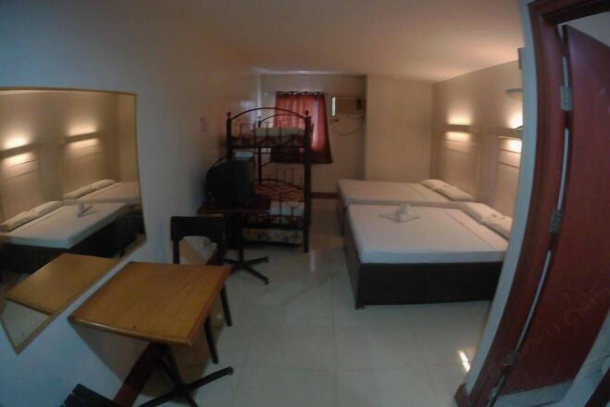 A small, compact room with two single beds, a desk, a chair, and a small table.