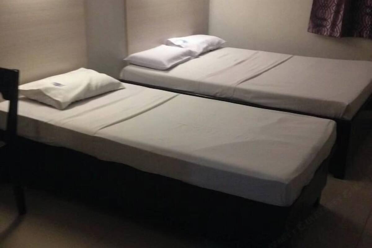 Two single beds with white linens in a room with plain walls and a curtain.