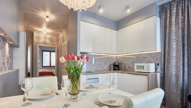 A modern dining area with a white table set for four, a vase of pink tulips, and a chandelier. - Apartamenty Sun & Snow Platan (Swinoujscie)