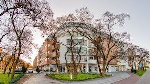 A multi-story building with a ground-level retail space, surrounded by trees and a bike lane. - Apartamenty Sun & Snow Platan (Swinoujscie)