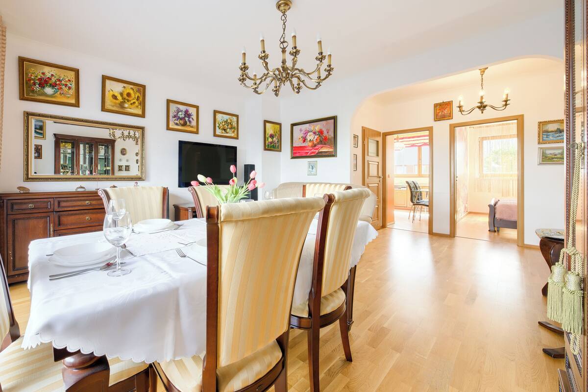 Comedor con una mesa dispuesta para cuatro, sillas de madera, una araña y varias obras de arte enmarcadas en las paredes.