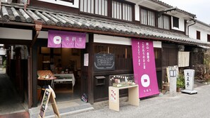 A traditional Japanese building with a tiled roof and wooden beams. There are signs in Japanese, a small table outside with items on it, and a chalkboard with writing. - Temari Hotel Yukikai (Kurashiki)