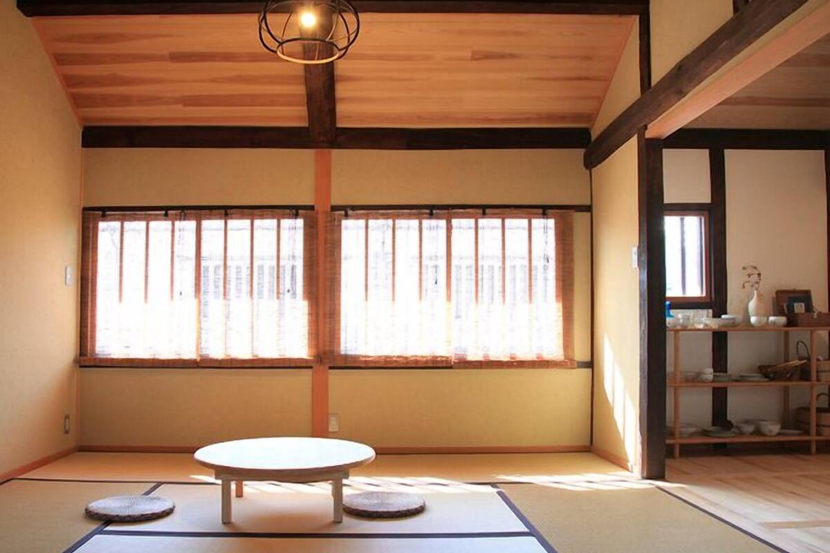 Habitació amb tatamis, una taula de tatami, dues almoinades, una làmpada penjant i una finestra amb persianes verticals.