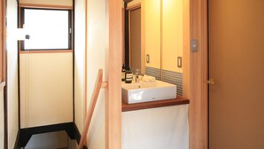 A bathroom with a wooden staircase, a sink with a mirror, and a window. - Temari Hotel Yukikai (Kurashiki)