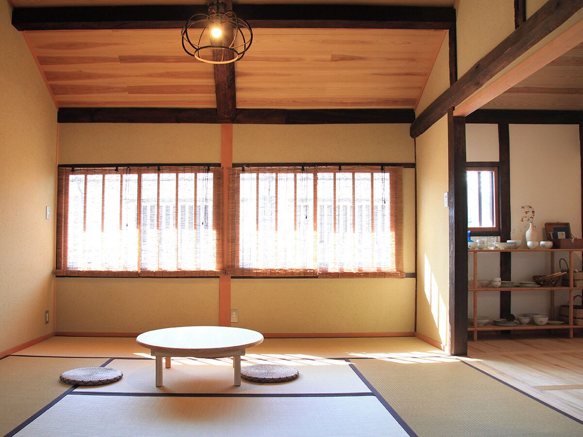 A traditional Japanese room with tatami flooring, a low table, and a window with sliding shoji doors.