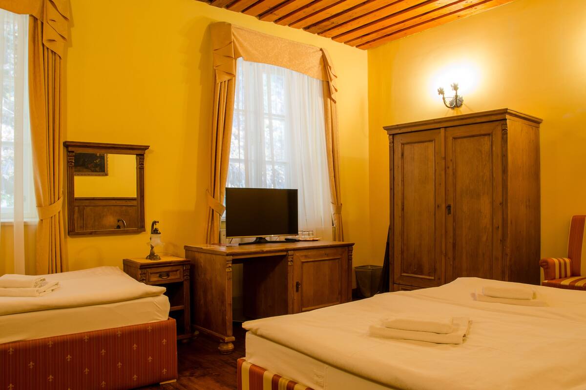 A hotel room with two beds, a desk with a TV, a wardrobe, and a window with curtains.