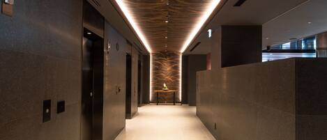 A modern hallway with a patterned ceiling, elevators, and a long corridor.