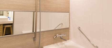 A modern bathroom with a large bathtub, a showerhead, and a handrail.