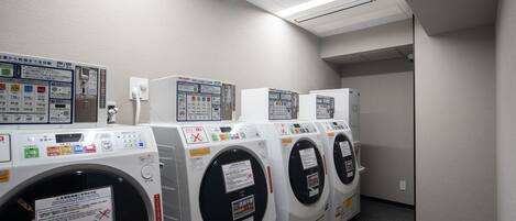 A row of front-loading washing machines in a laundry room with control panels and safety instructions.