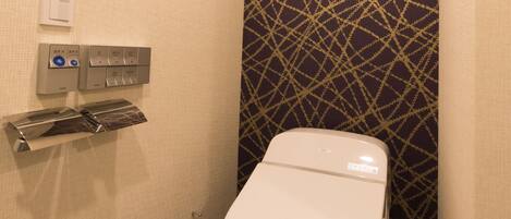 A small, compact bathroom with a white toilet, a towel dispenser, and a hand dryer.