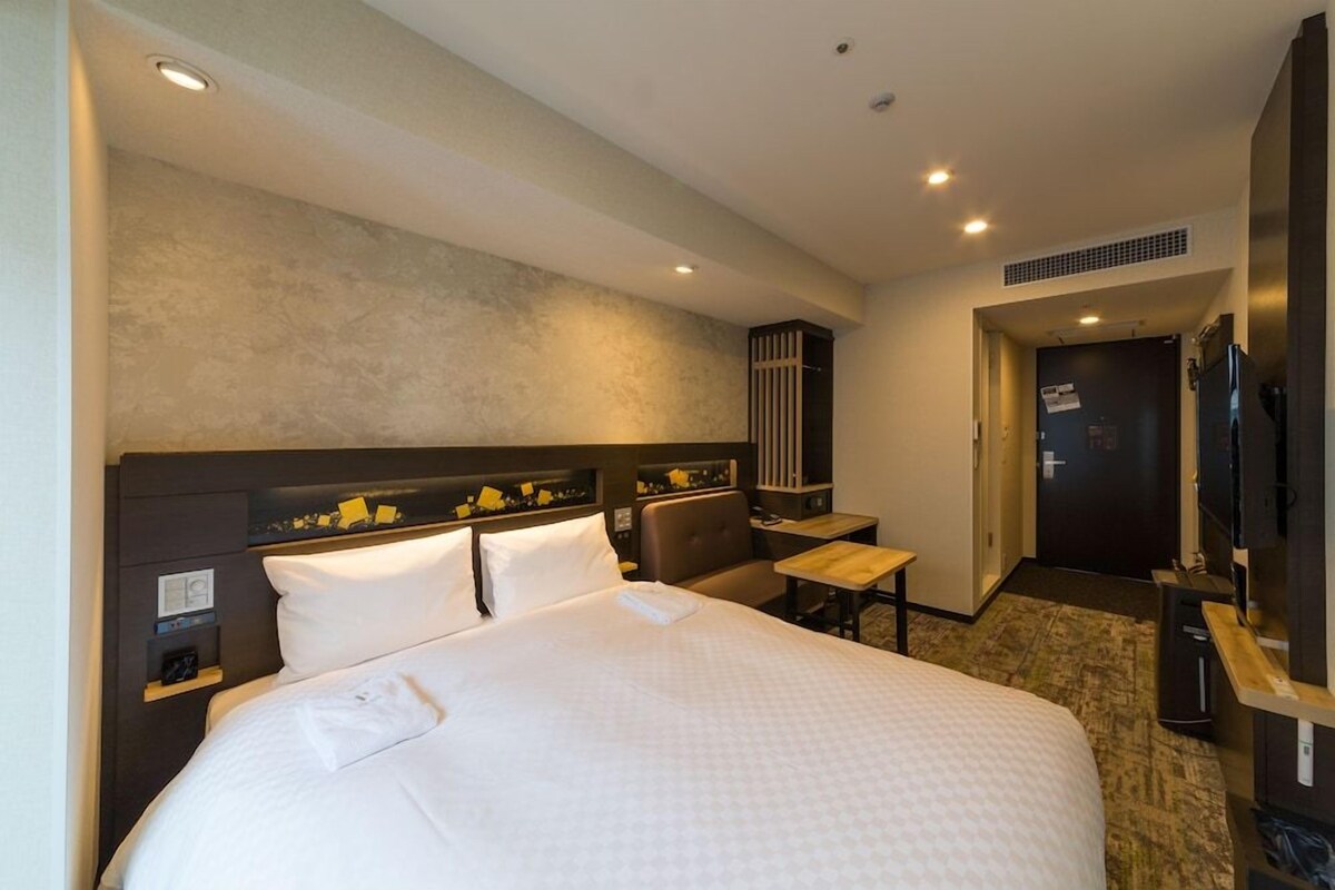A hotel room with a large bed, a desk, a television, and a wardrobe.