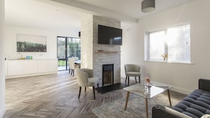 A spacious living area with a fireplace, modern furniture, and a large TV mounted on a stone wall. - Killester Self Catering Cottage (Dublin)
