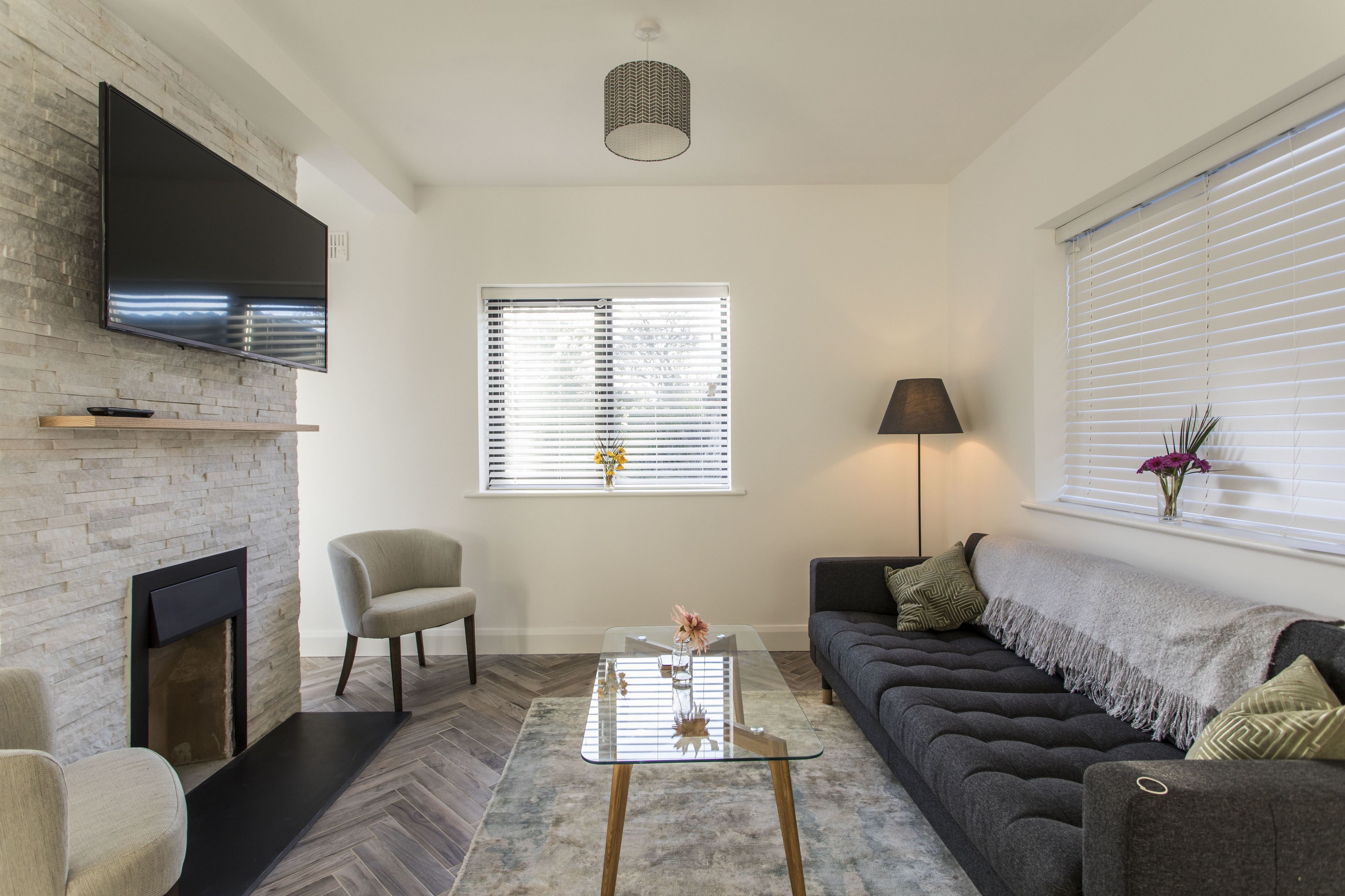 Een moderne woonkamer met een open haard, een flatscreen televisie bevestigd aan een bakstenen muur, een bank, een salontafel en een lamp.