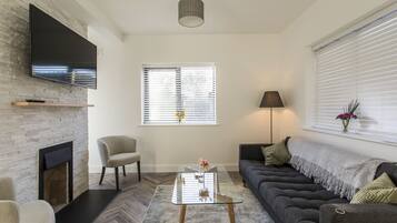 Een moderne woonkamer met een open haard, een flatscreen televisie bevestigd aan een bakstenen muur, een bank, een salontafel en een lamp.