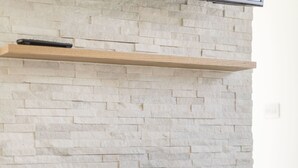 A modern fireplace with a stone facade, a black mantel, and a remote control on the shelf above. - Killester Self Catering Cottage (Dublin)