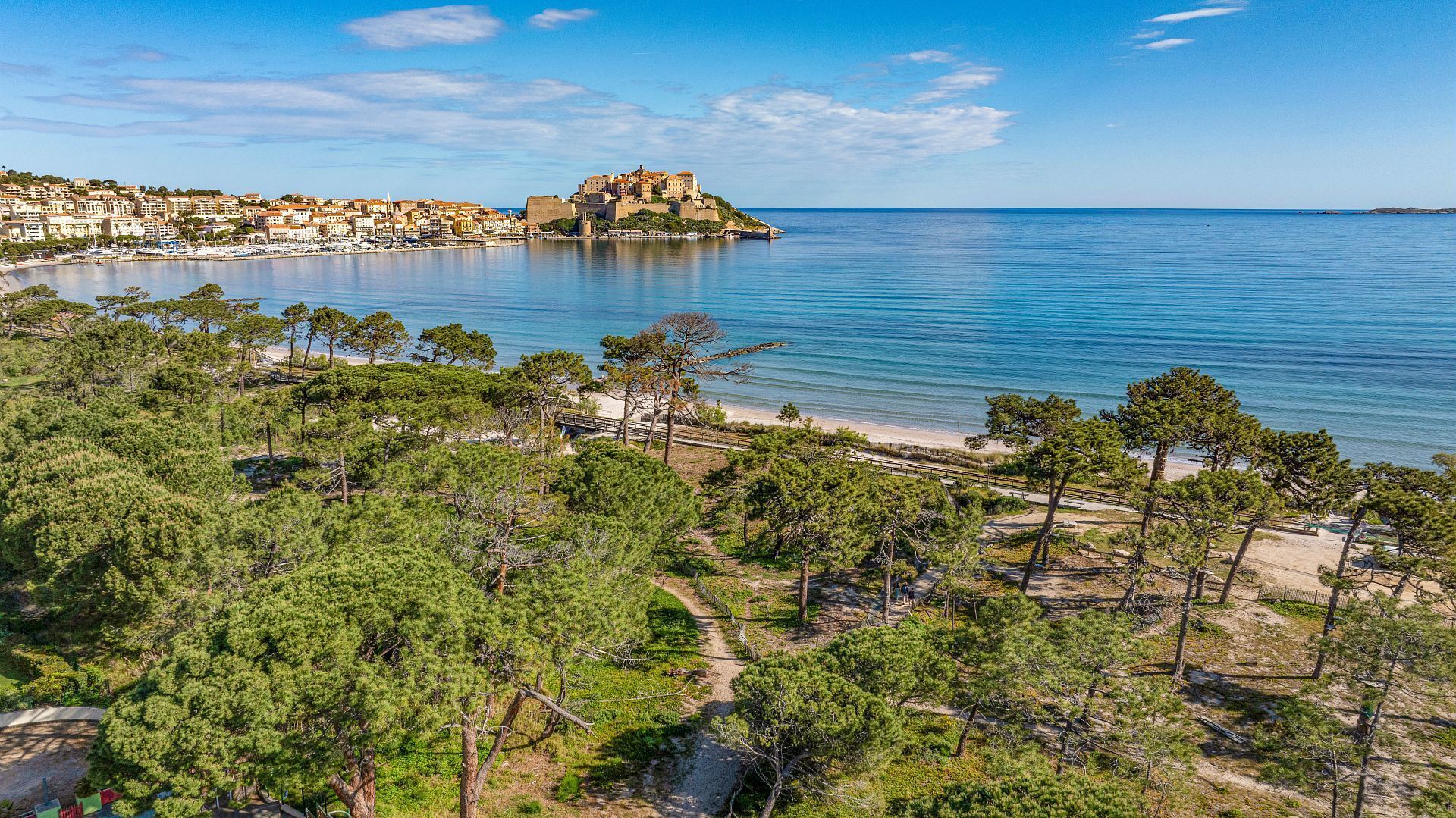 Une ville côtière dotée d’un fort historique, d’un ciel dégagé et d’une plage bordée de pins.