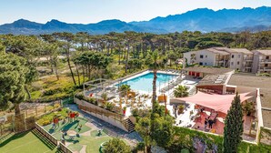 A pool area with a view of mountains, surrounded by greenery and a building with multiple floors. - Village Club Miléade Calvi (Calvi)