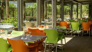 An outdoor dining area with tables and chairs, large windows, and a view of greenery. - Village Club Miléade Calvi (Calvi)