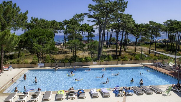 A swimming pool with people swimming and lounging, surrounded by trees and a view of the sea. - Village Club Miléade Calvi (Calvi)