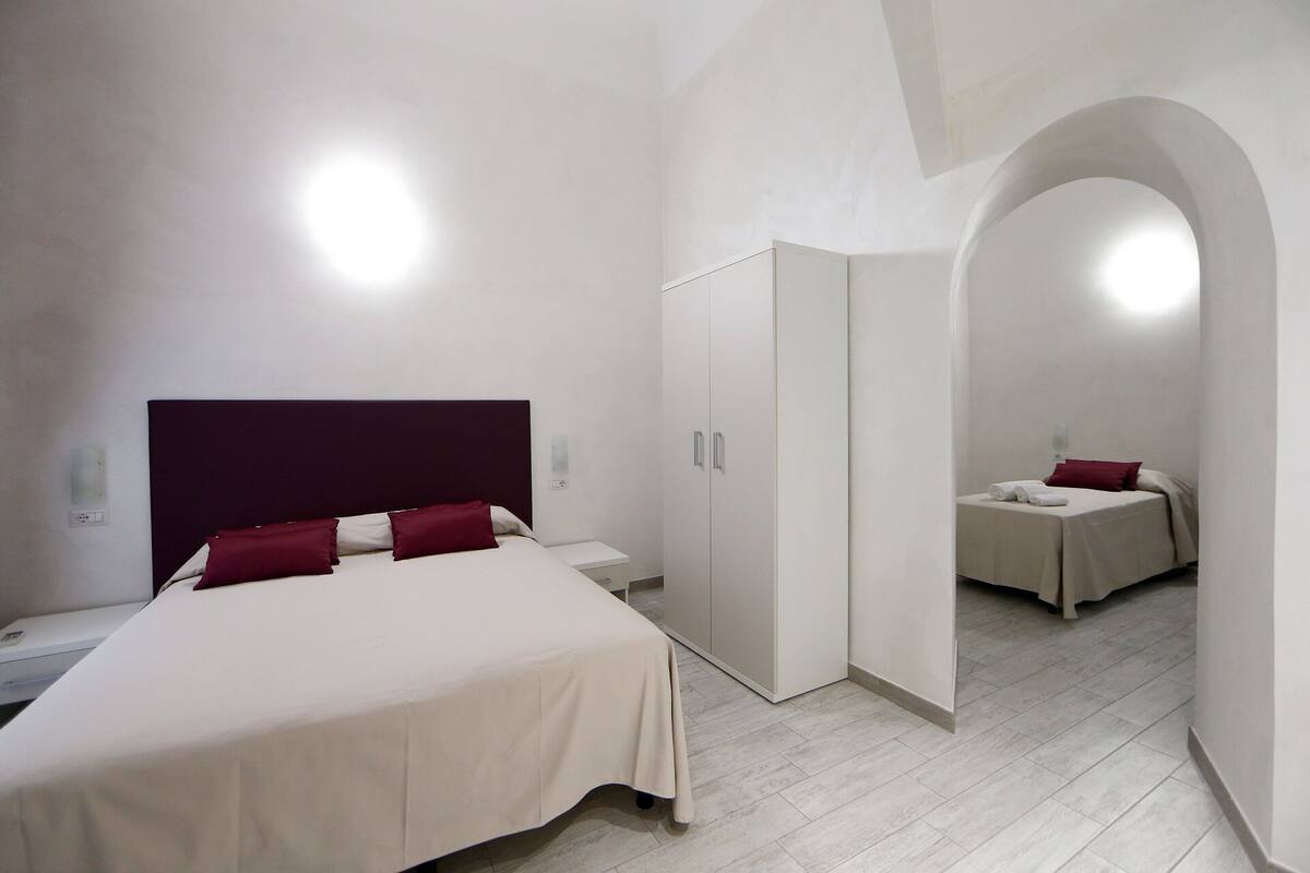 A modern hotel room with a large bed, a wardrobe, and a small seating area.
