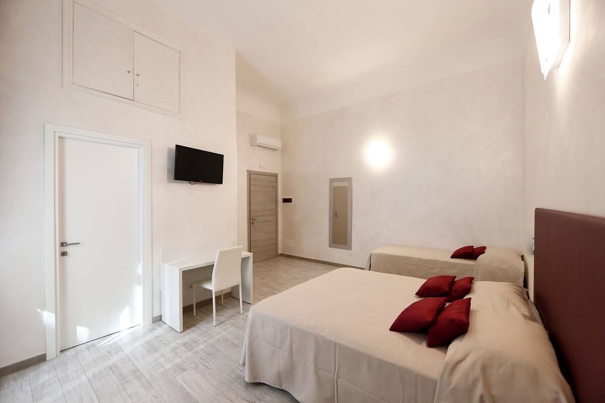 A hotel room with a bed, a desk, a chair, a TV, and a mirror.