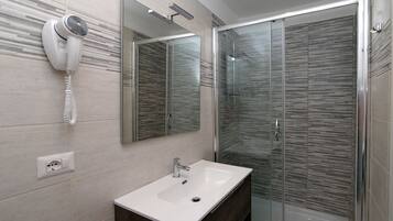 Un bagno moderno con box doccia in vetro, lavabo incassato e asciugacapelli fissato alla parete.